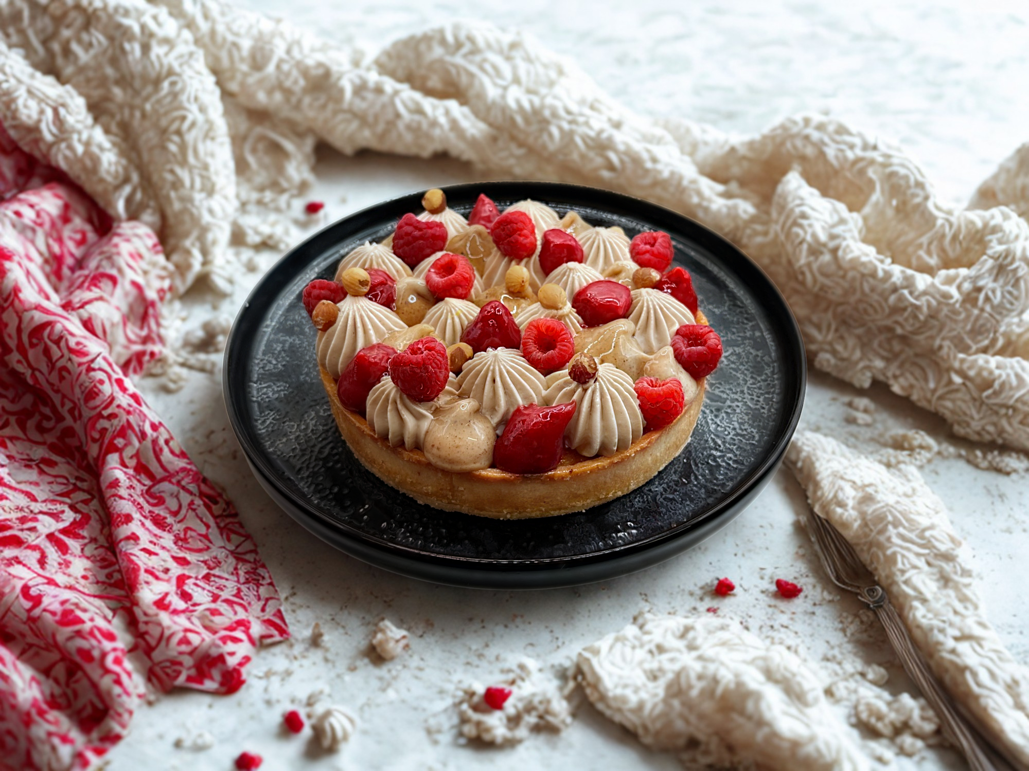 Cette tarte associe une pâte sucrée croustillante, un financier à la noisette, un confit de framboises acidulé, un crémeux praliné fondant et une chantilly au chocolat au lait origine Madagascar.